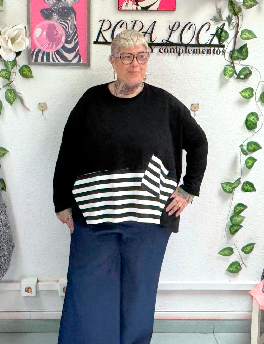 Chica posando con una sudadera color negro, con detalle de faldón y parche en rayas blancas y negra. Abertura lateral. Talla curvy.